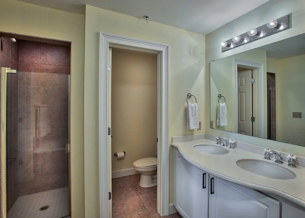 A bathroom with two sinks , a toilet , and a walk in shower.
