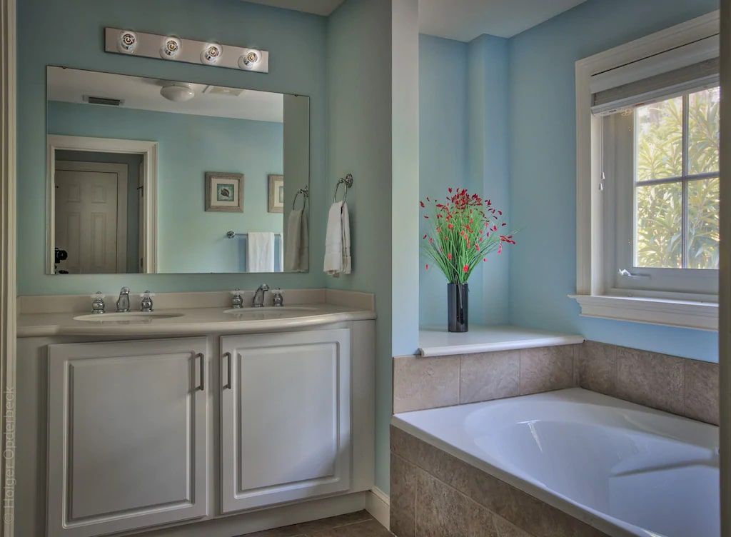 A bathroom with a tub , sink , mirror and window.