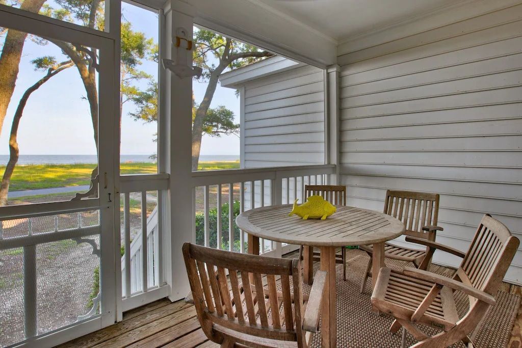 A screened in porch with a table and chairs and a view of the ocean.