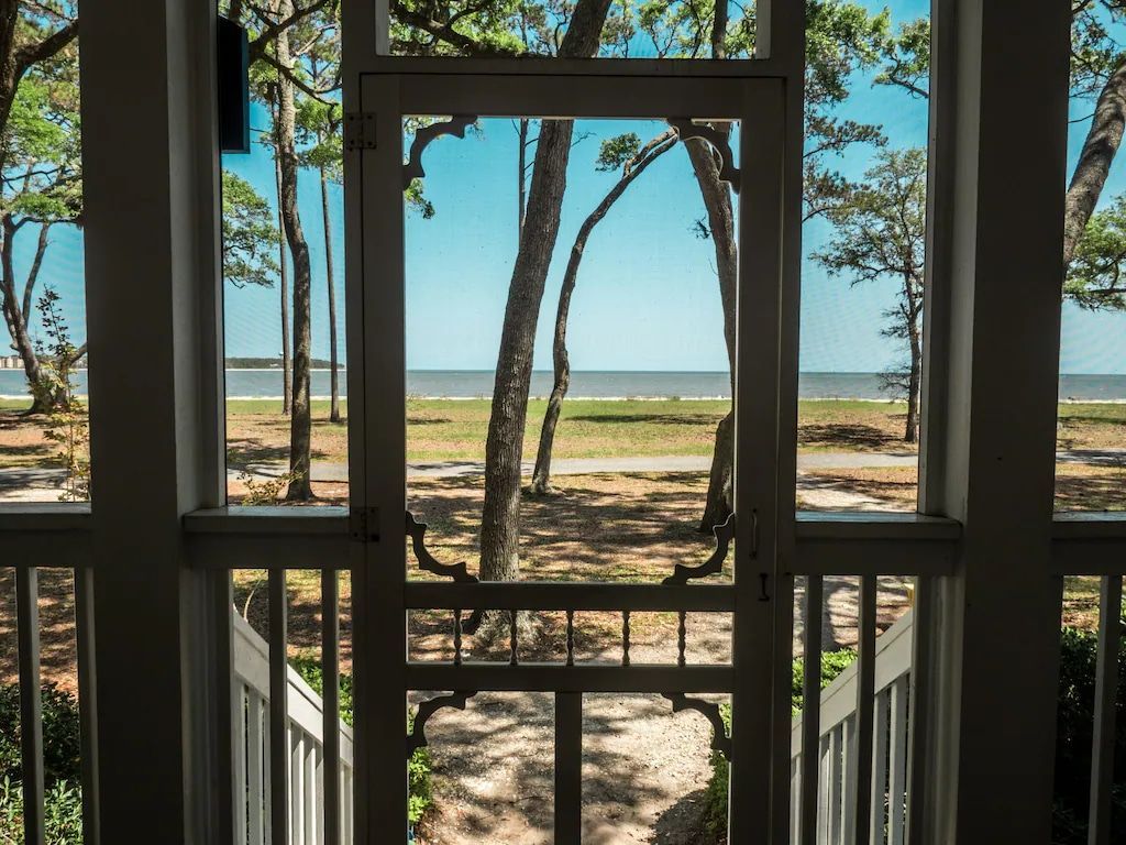 A screened in porch with a view of the ocean and trees.
