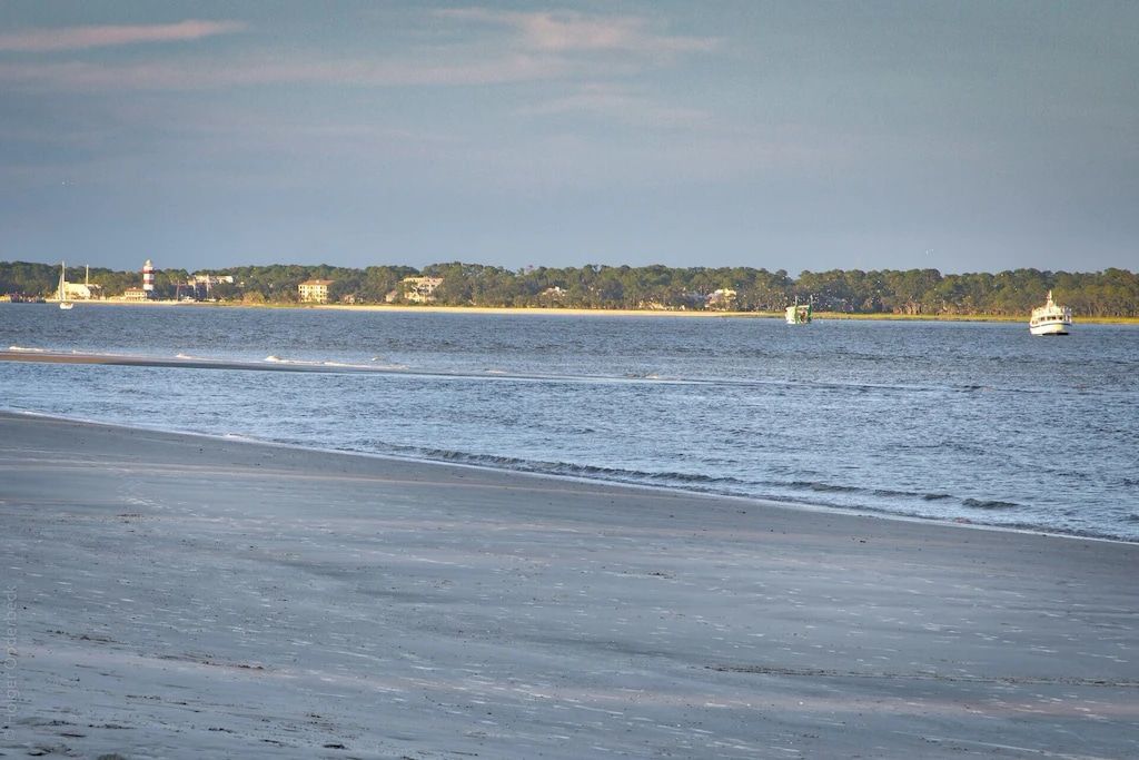 A boat is floating on top of a body of water near a beach.