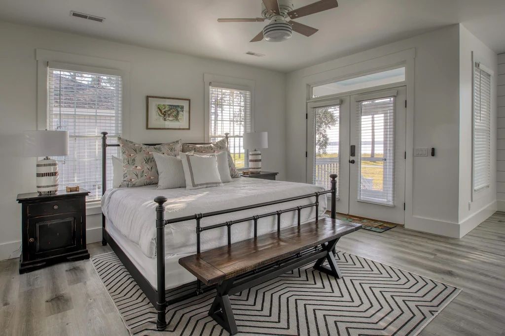 A bedroom with a king size bed , a bench , a rug and a ceiling fan.