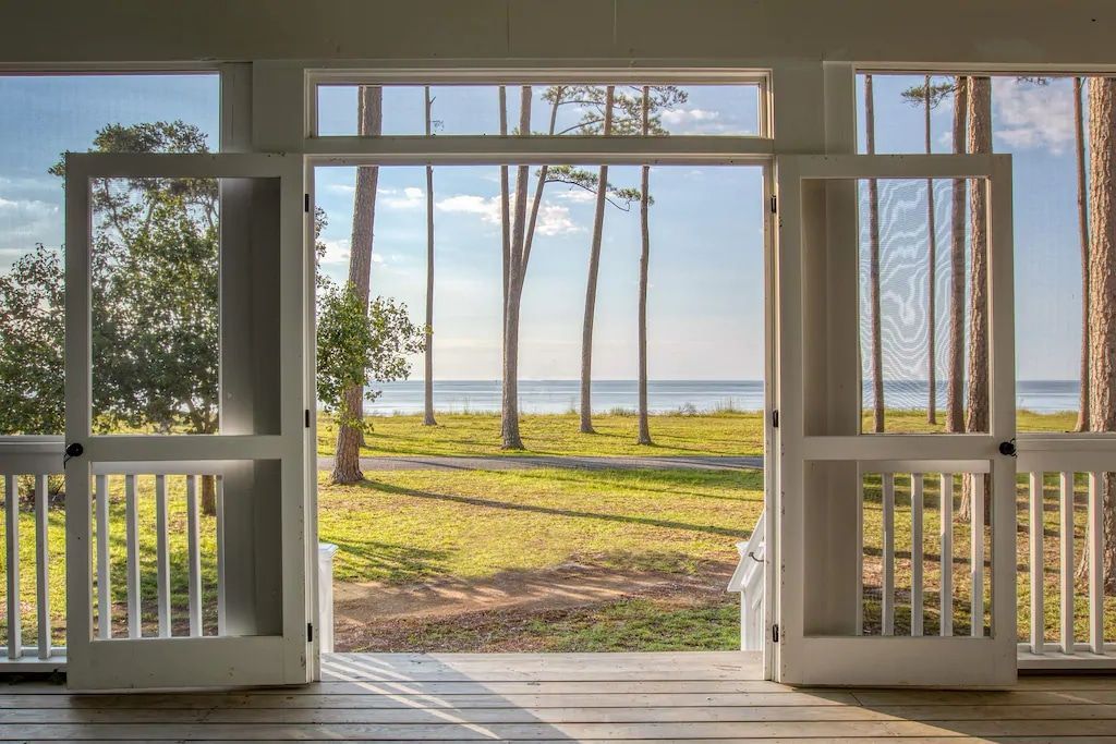 A screened in porch with a view of the ocean and trees.