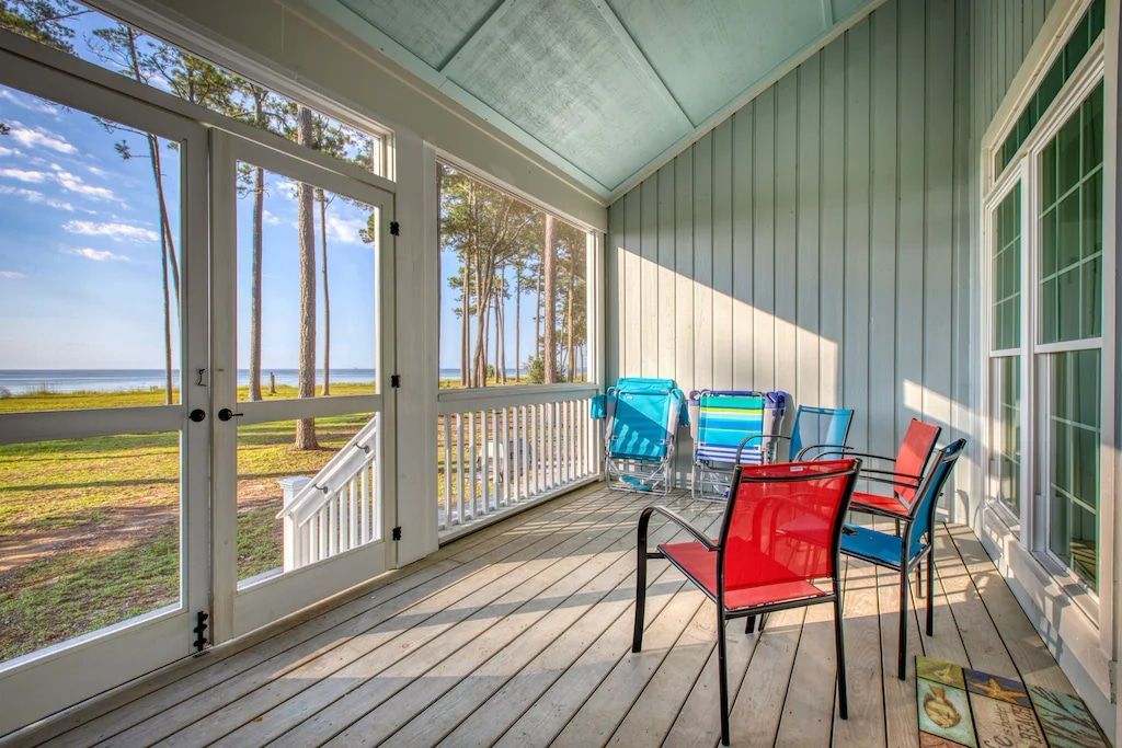 A screened in porch with a table and chairs and a view of the ocean.