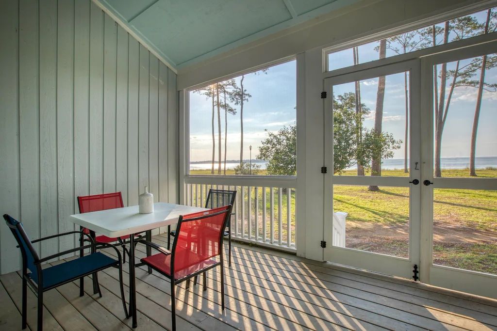 A screened in porch with a table and chairs and a view of the ocean.