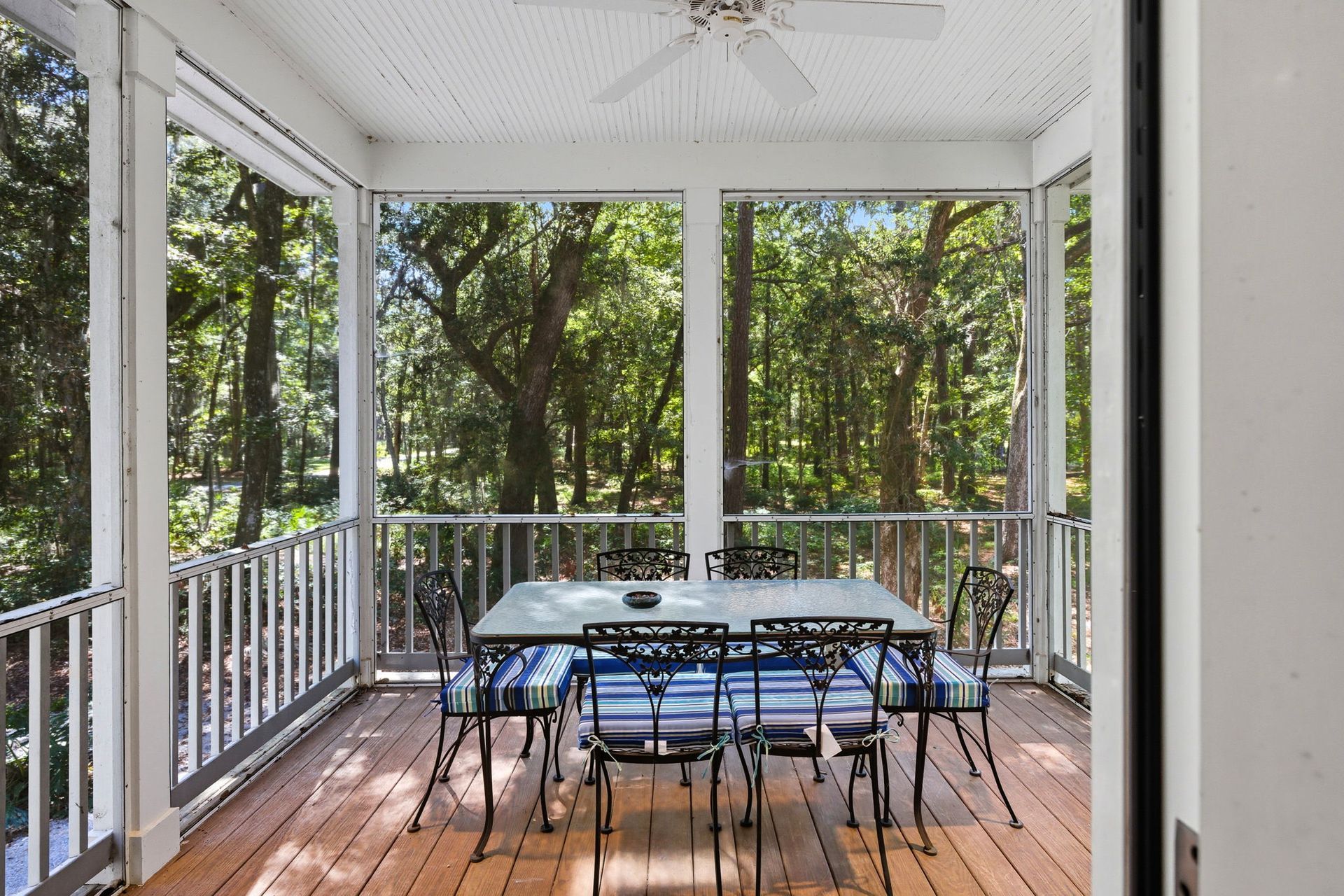 A screened in porch with chairs and a view of the ocean.