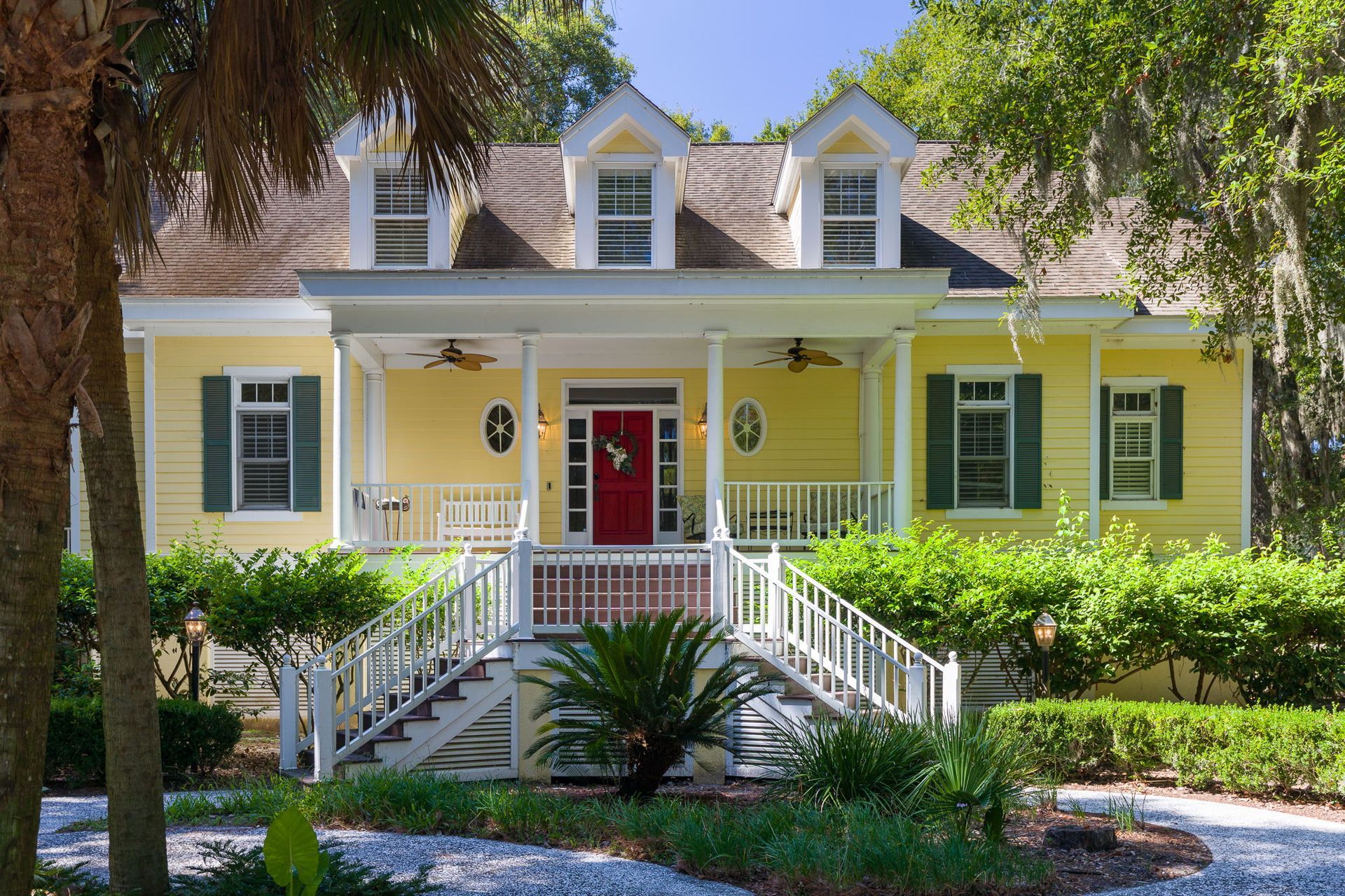 A white house with a large porch is surrounded by trees.