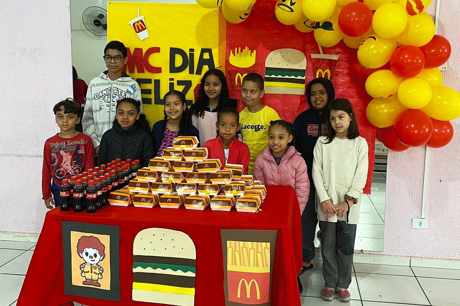 Um grupo de crianças posa em frente a uma placa do McDonald's
