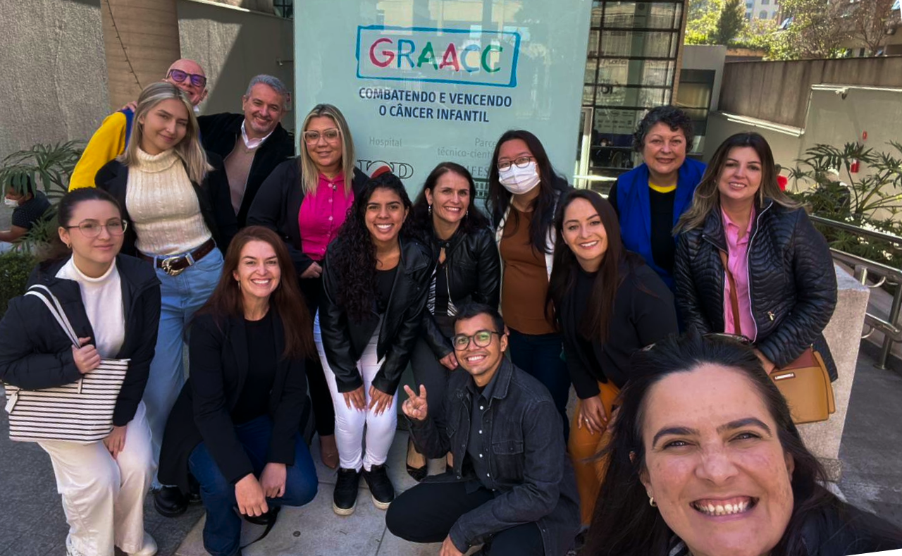 Um grupo de pessoas posando para uma foto em frente a uma placa graacc
