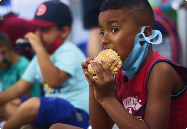A boy wearing a mask is eating a hamburger