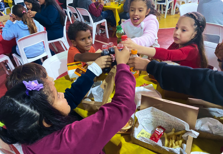 Um grupo de crianças está sentado à mesa brindando com coca cola