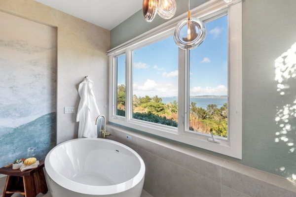 Master bathroom with freestanding white oval soaking tub positioned in front of expansive multi-pane windows overlooking