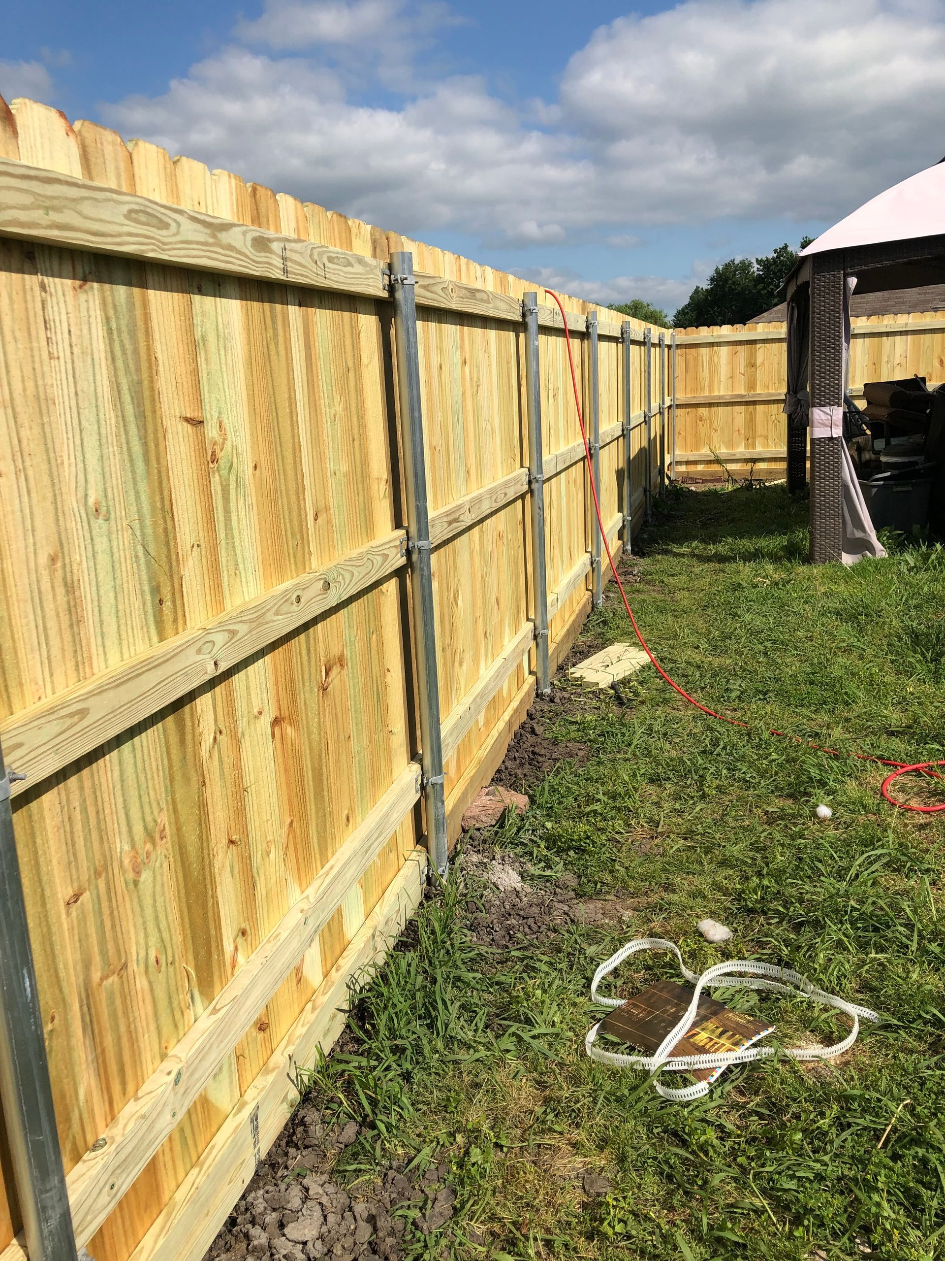 New wooden fence along a grassy backyard with a house and hose on the right