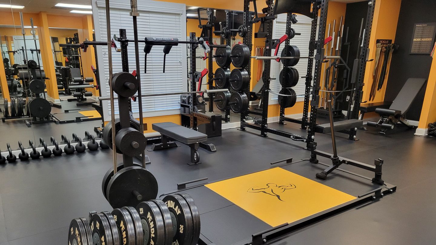 Gym with weight racks, barbells, benches, and dumbbells on a gray floor with yellow platforms.