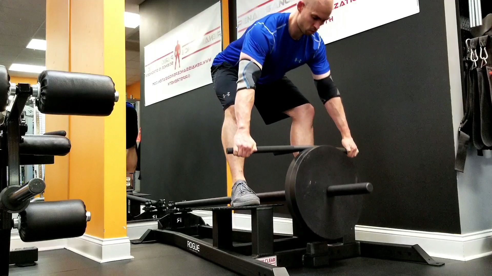 Man lifting a barbell in a gym, bent over a deadlift platform with weight plates on each side