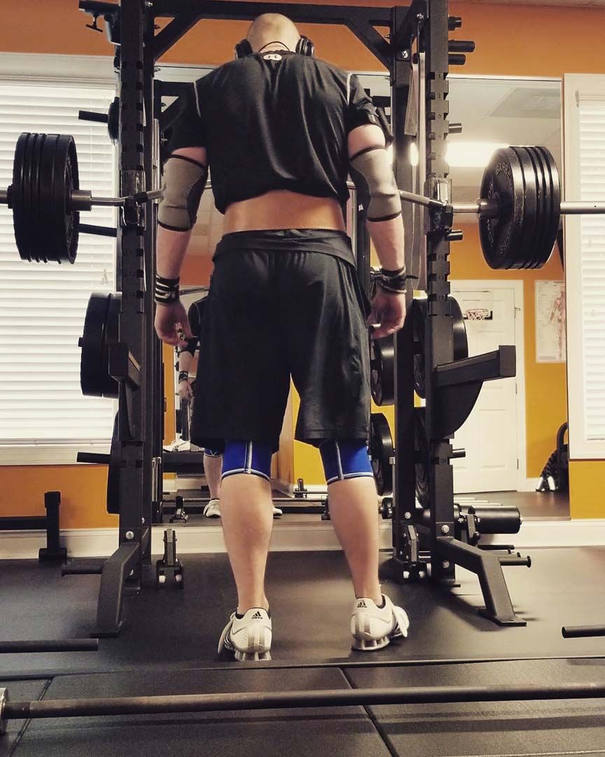 Person doing a deadlift in a gym with a barbell and weight plates.