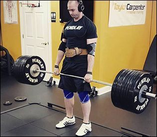 Powerlifter deadlifting a heavily loaded barbell in a gym, wearing a belt, knee sleeves, and headphones