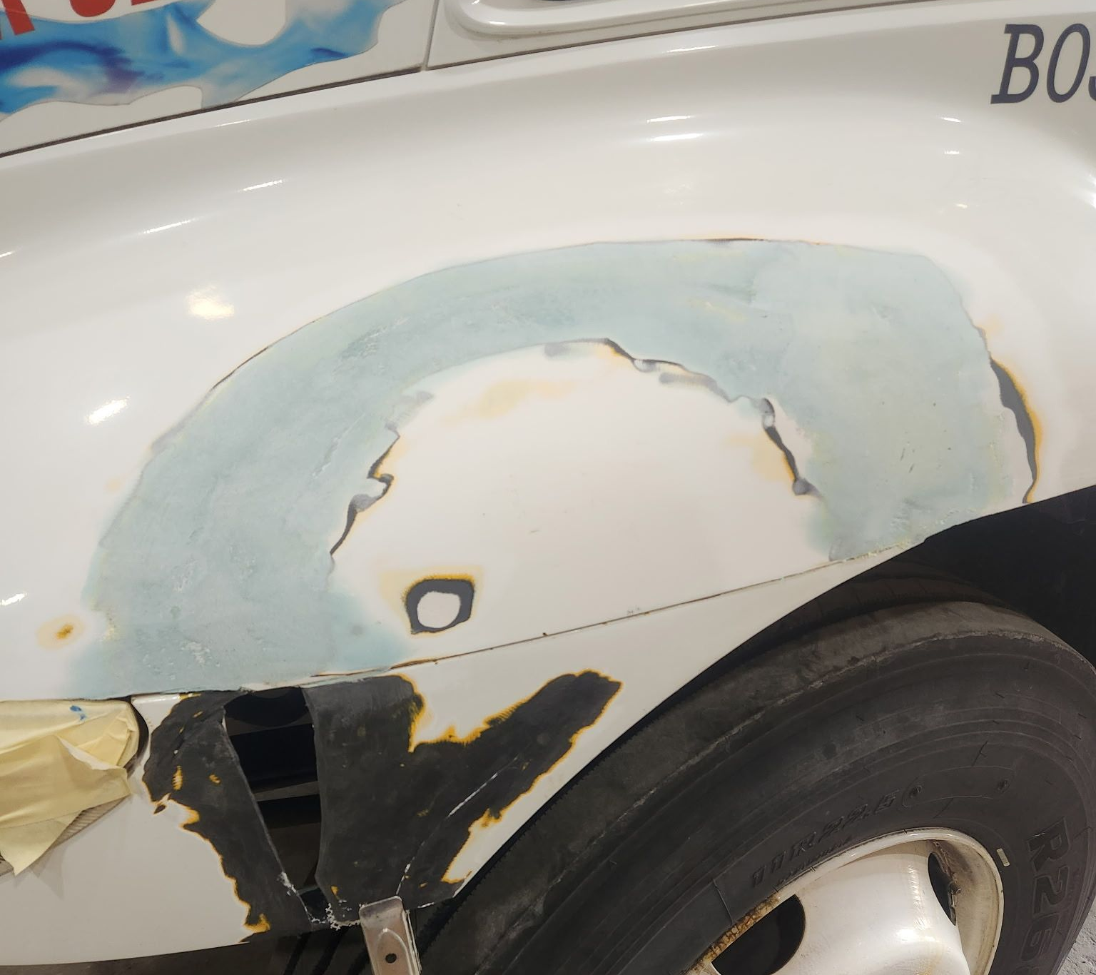 White car fender undergoing bodywork repair, with primer and putty applied.