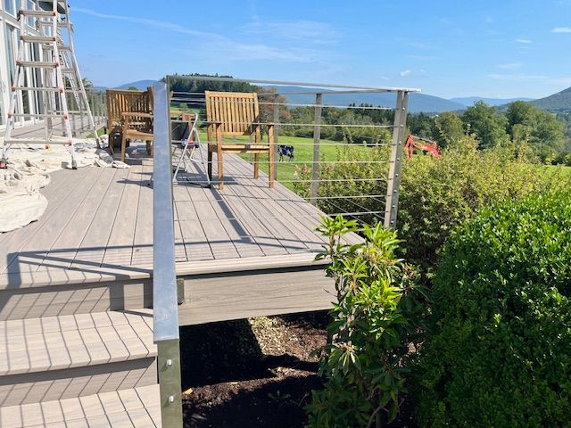Deck with stainless steel railing and chairs overlooking a green field and mountains.