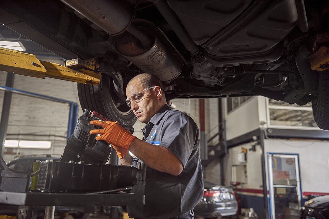 Mechanic in orange gloves inspecting a car engine on a lift in an auto repair shop