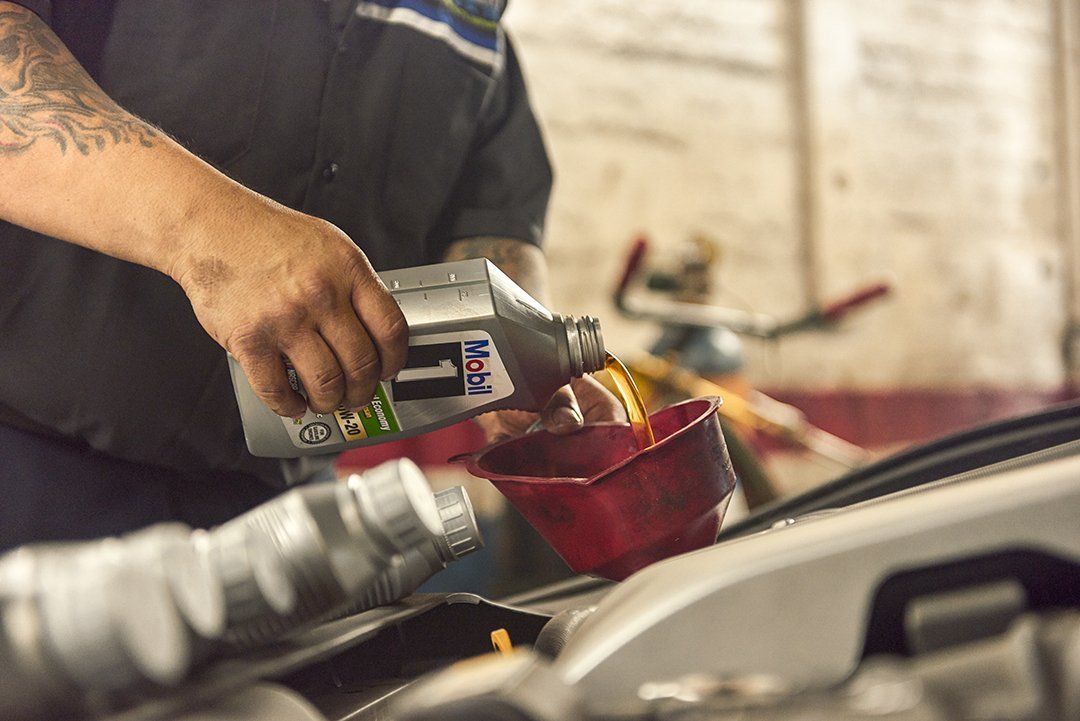 Mechanic pouring oil into a red car engine at a repair shop