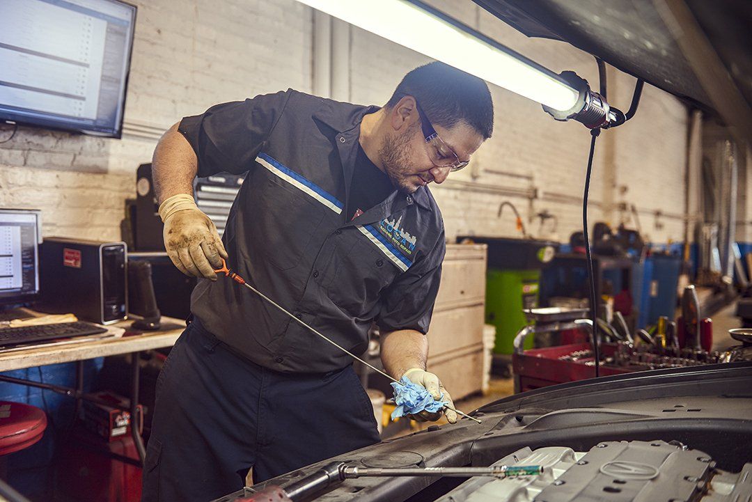 Mechanic in a garage working under a car hood with tools, wearing gloves and dark work clothes