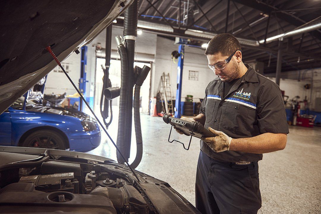Mechanic inspecting a car engine in a garage with a blue car in the background