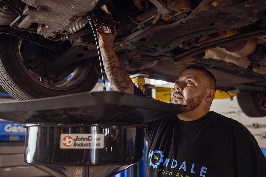 Mechanic inspecting the underside of a car while oil drains into a pan beneath it