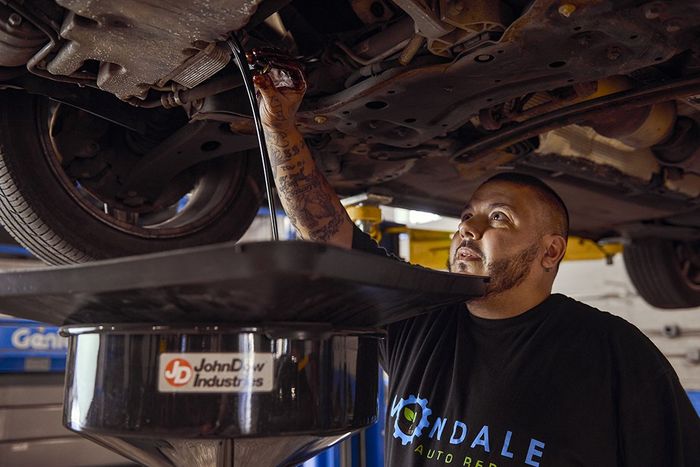 Mechanic drains oil from a car underside into a black pan in an auto repair shop.