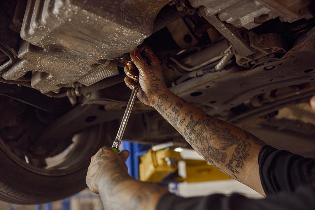 Mechanic draining oil from a car beneath a vehicle on a lift