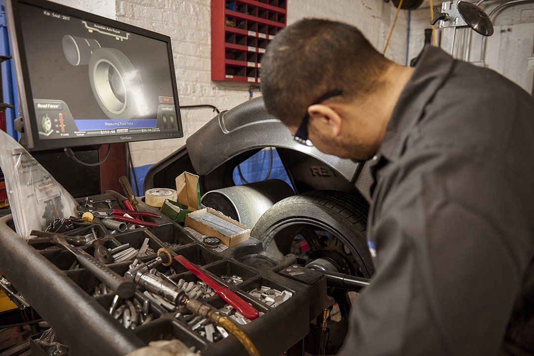 Mechanic inspecting a car engine with a laptop on a workshop bench