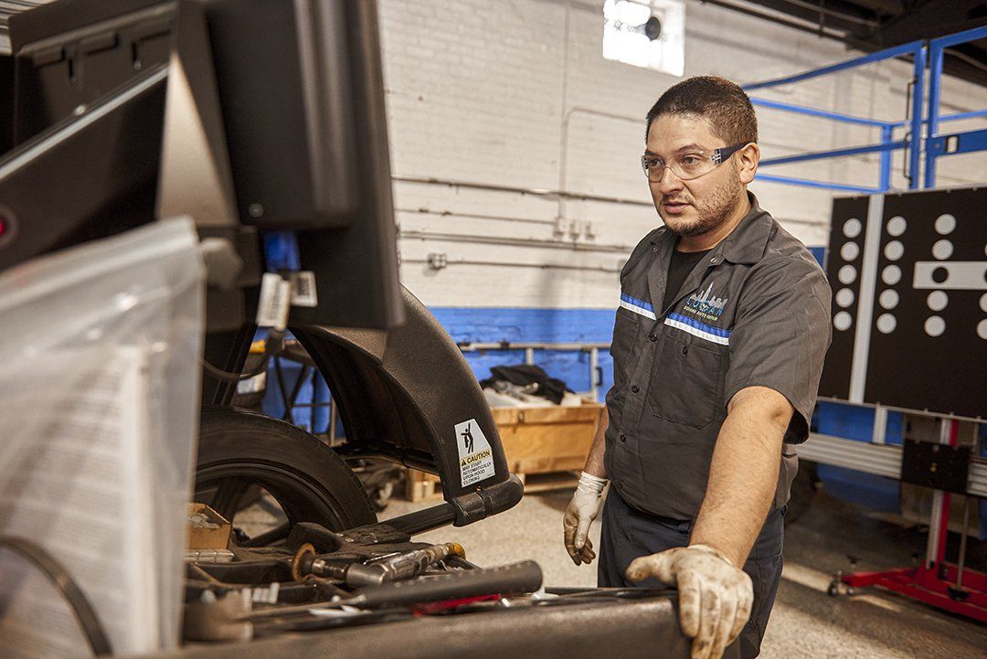 Mechanic in a workshop inspecting a vehicle on a lift, with tools on a workbench.