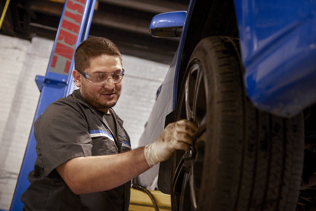 Mechanic inspecting a tire on a blue vehicle in a repair shop