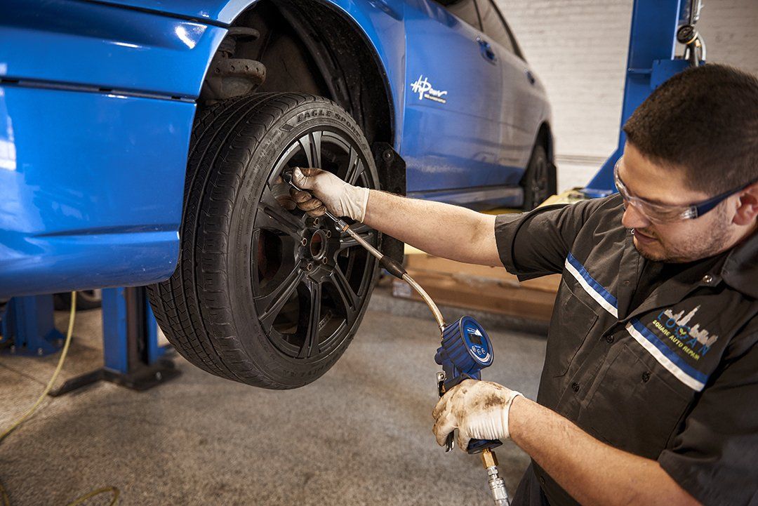 Mechanic inspecting the tire of a blue car in a garage with a wrench