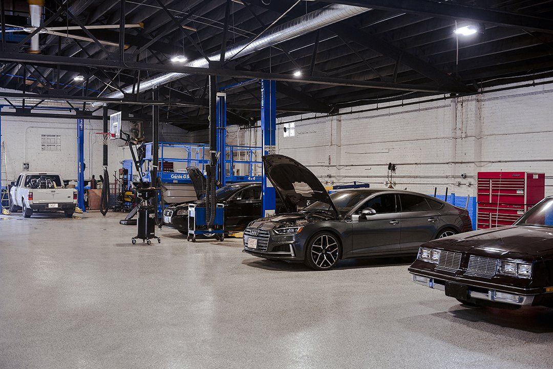 Auto repair shop with several cars, one lifted on a blue hoist and another with its hood open