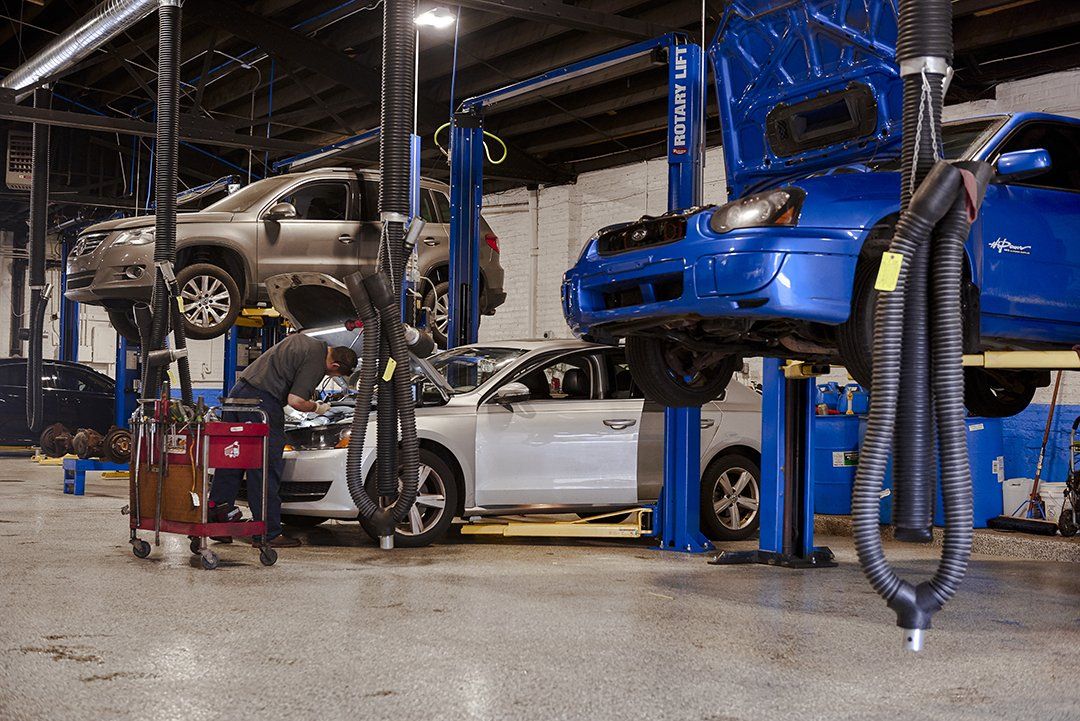Cars on lifts in an auto repair shop, including a blue vehicle and a silver car.