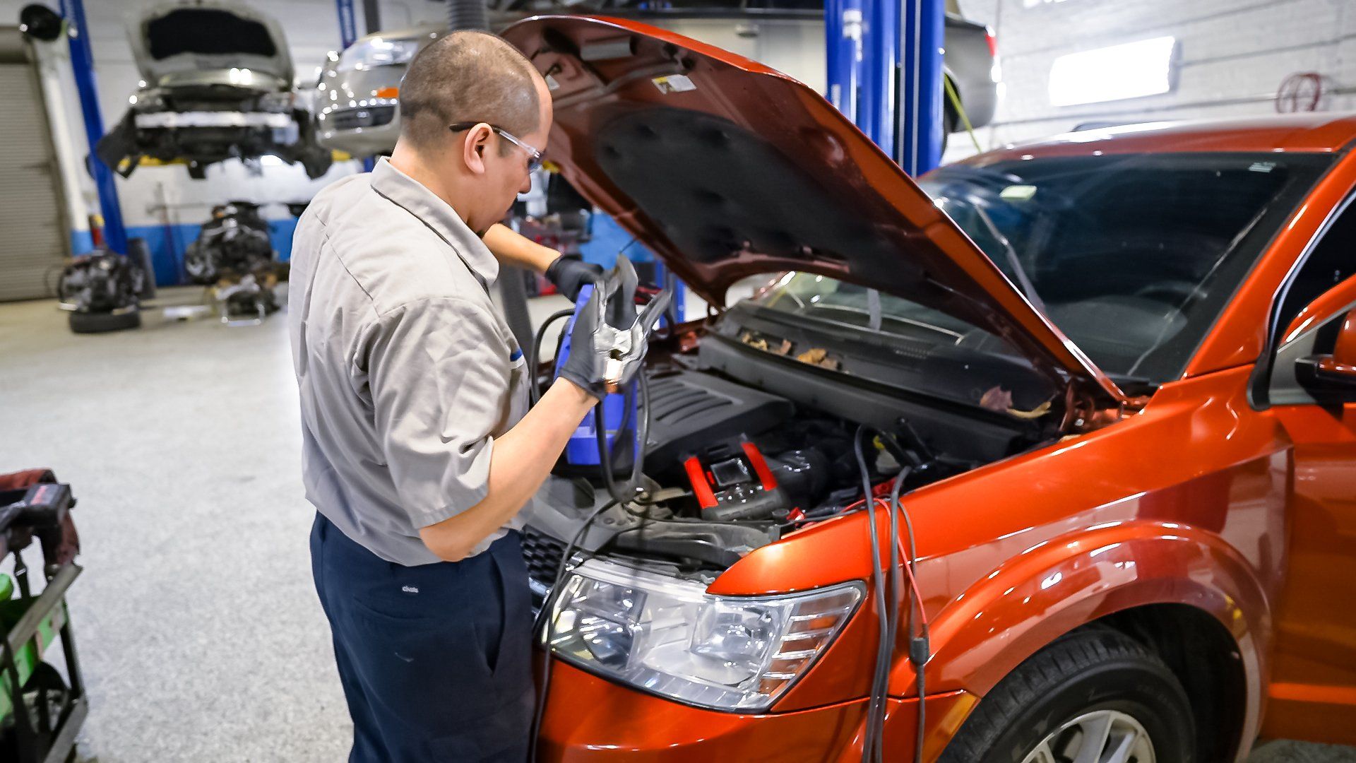 Mechanic inspecting engine bay of an orange SUV in an auto repair shop