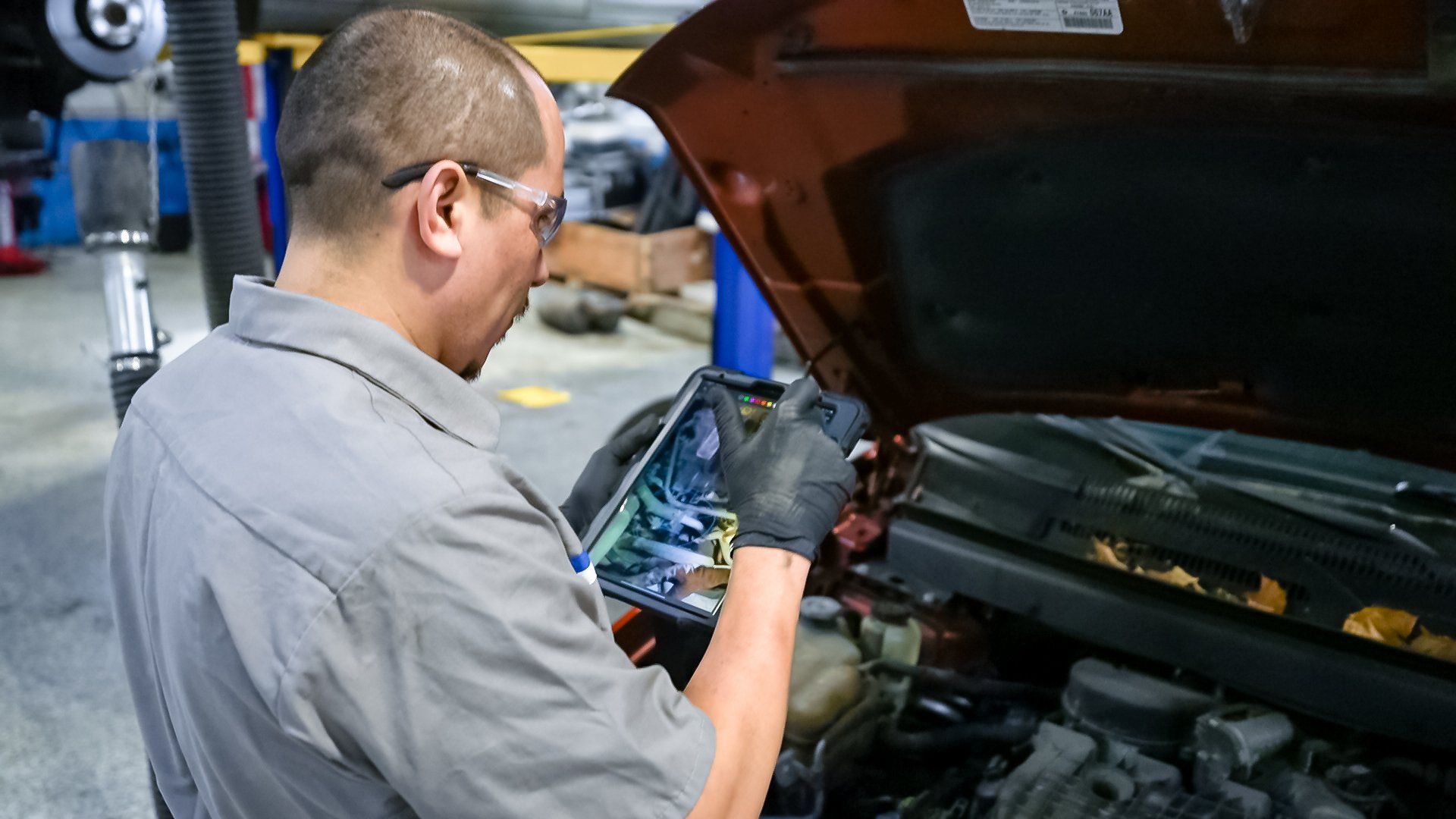 Mechanic inspecting a car engine bay with the hood open while holding a diagnostic device