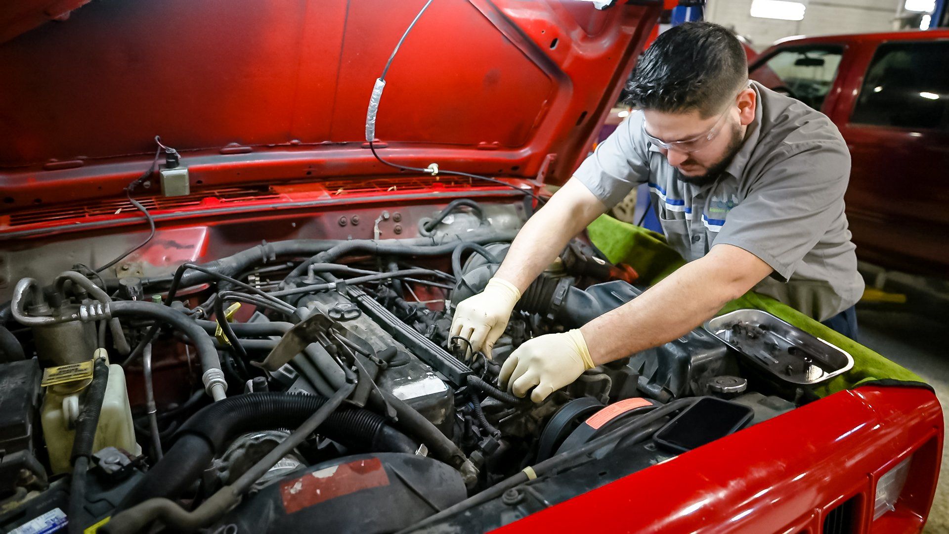 Mechanic working under the hood of a red car in a garage, inspecting the engine.