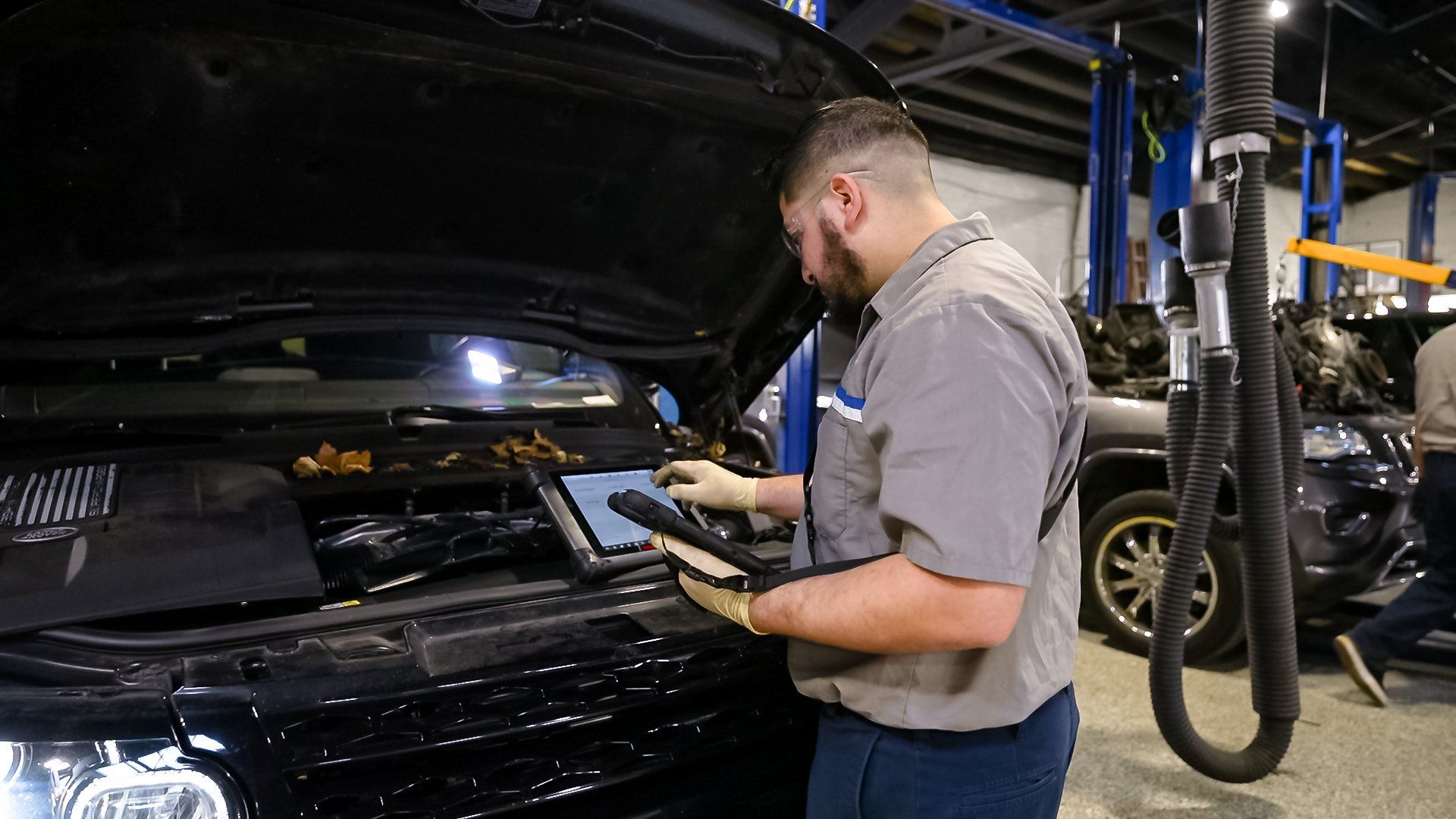 Mechanic inspecting a car engine in an auto repair shop with the hood open.