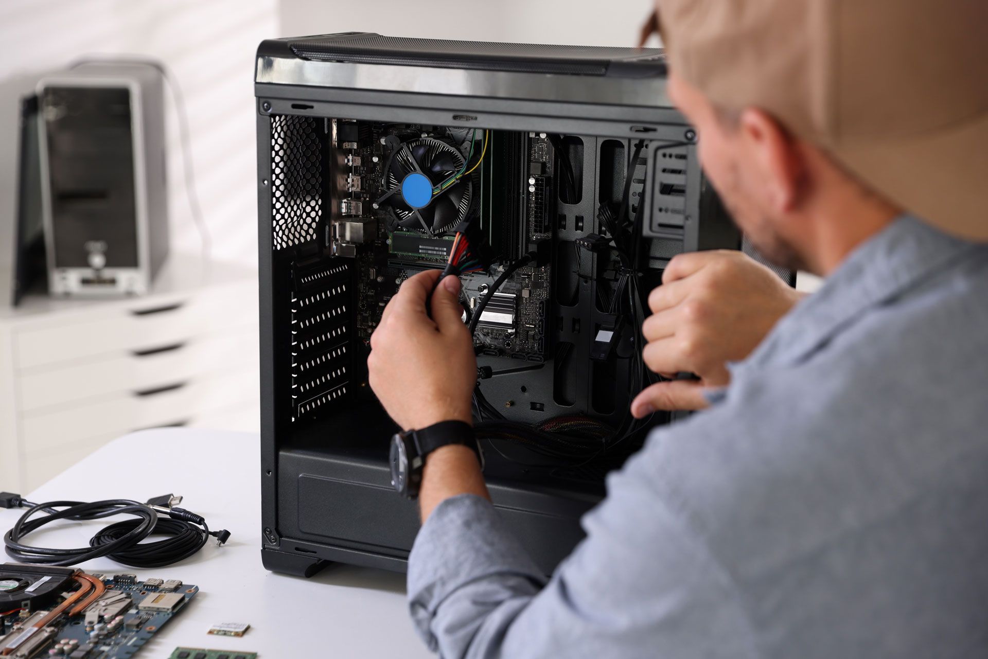 Person working on a desktop computer, connecting wires. PC case open on a white table.