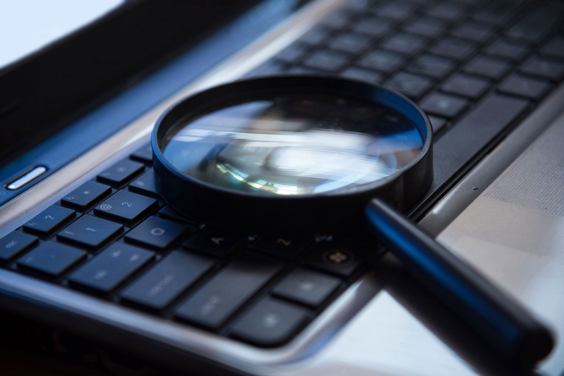 Magnifying glass on laptop keyboard, highlighting keys.