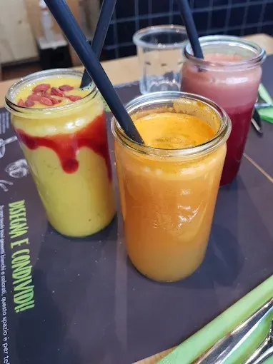 Tre frullati colorati in barattoli di vetro con cannucce su un tavolo.