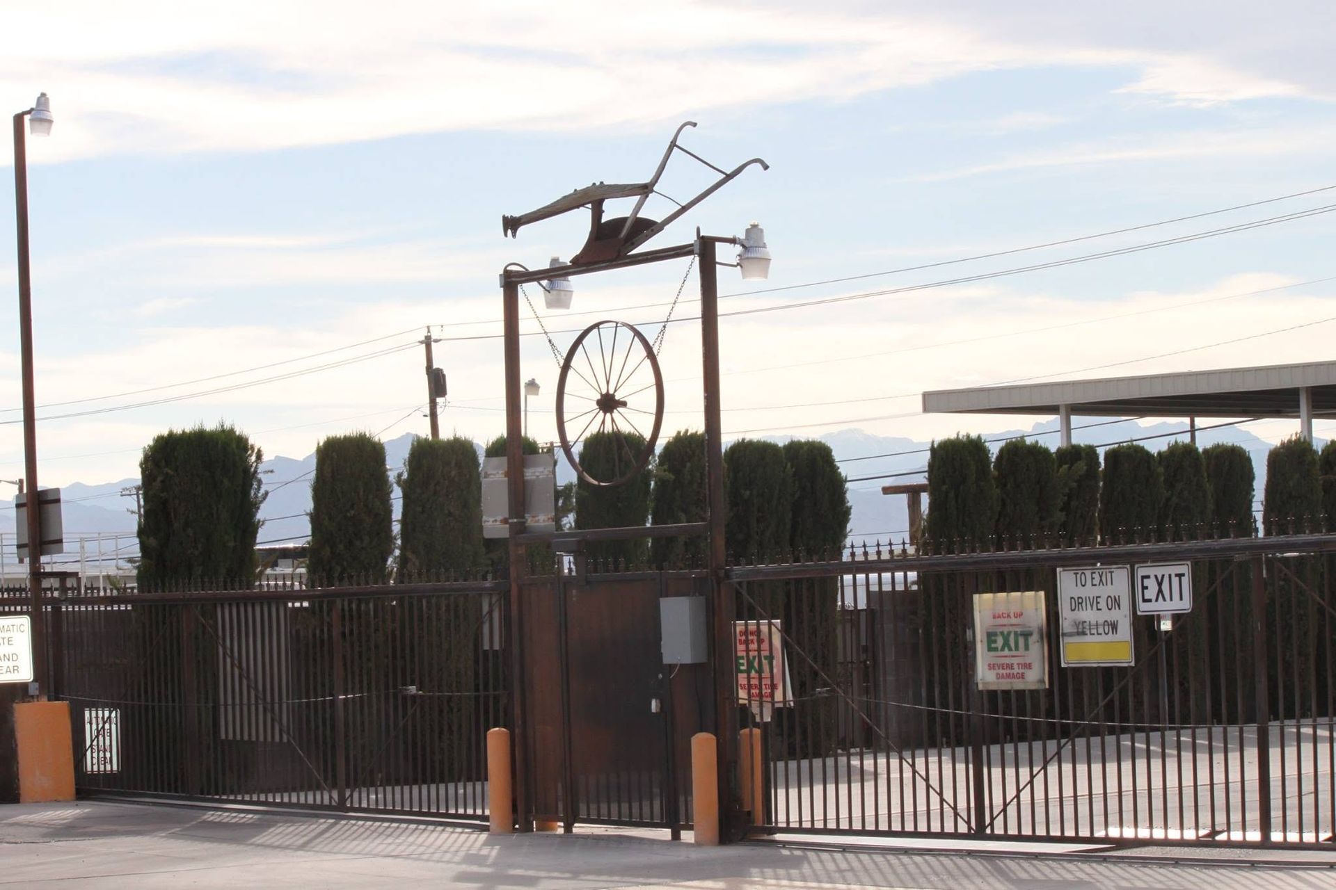 Gated entrance with tall hedges, a large bird sculpture, and a Ferris wheel in the background at dusk