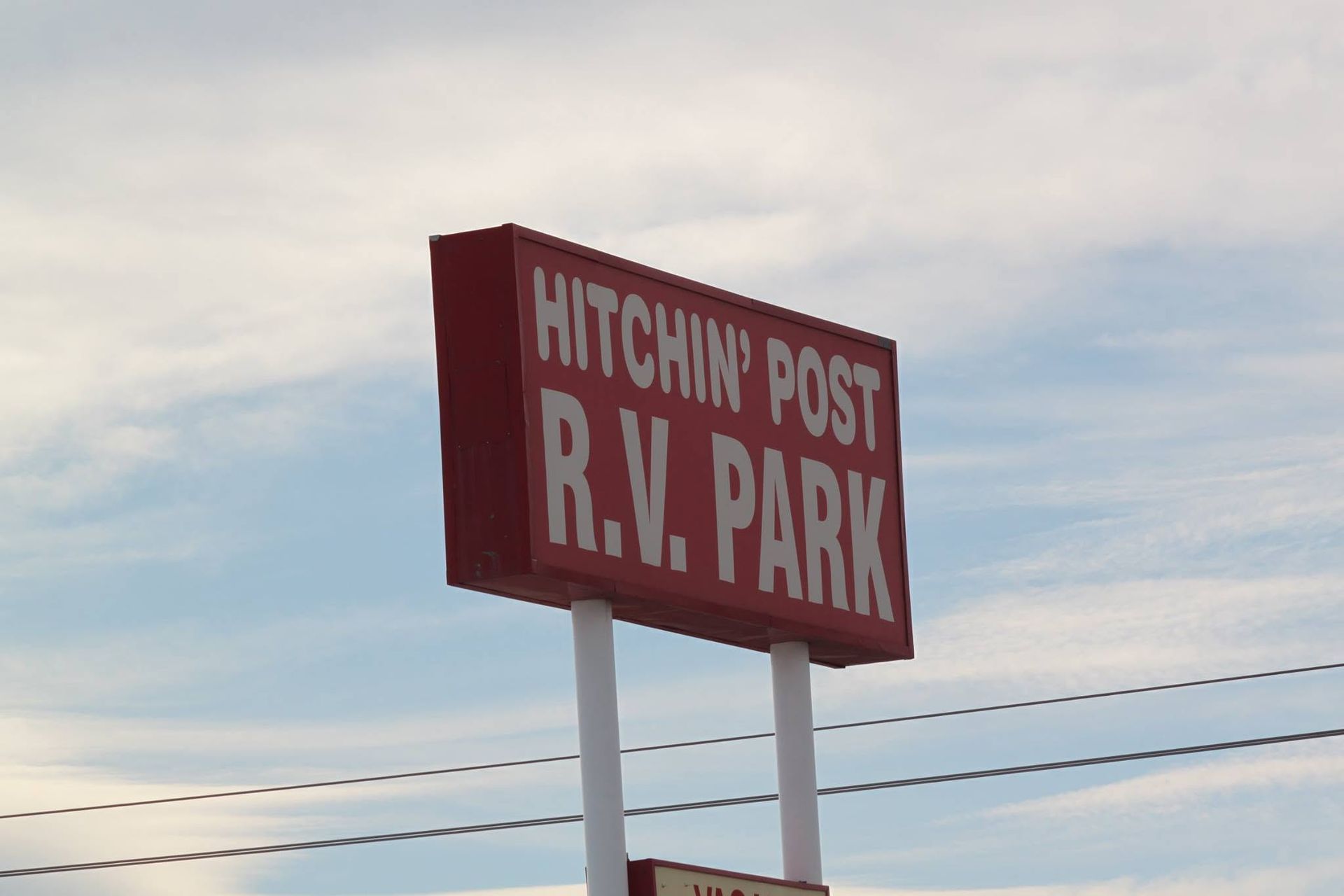 A truck with a lift repairs the Watchin' Post R.V. Park sign, against a blue sky.