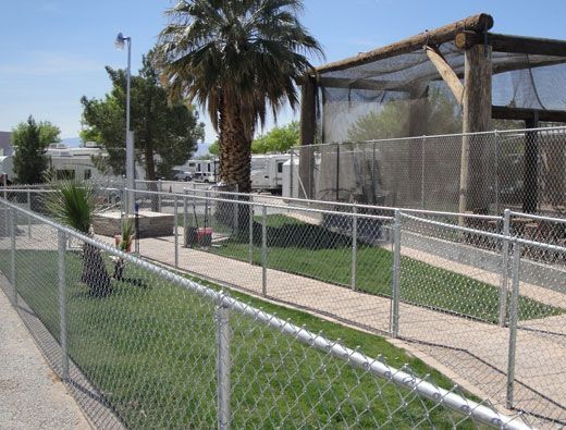 A dog park with chain-link fences, grass, a walkway, and a shaded structure.