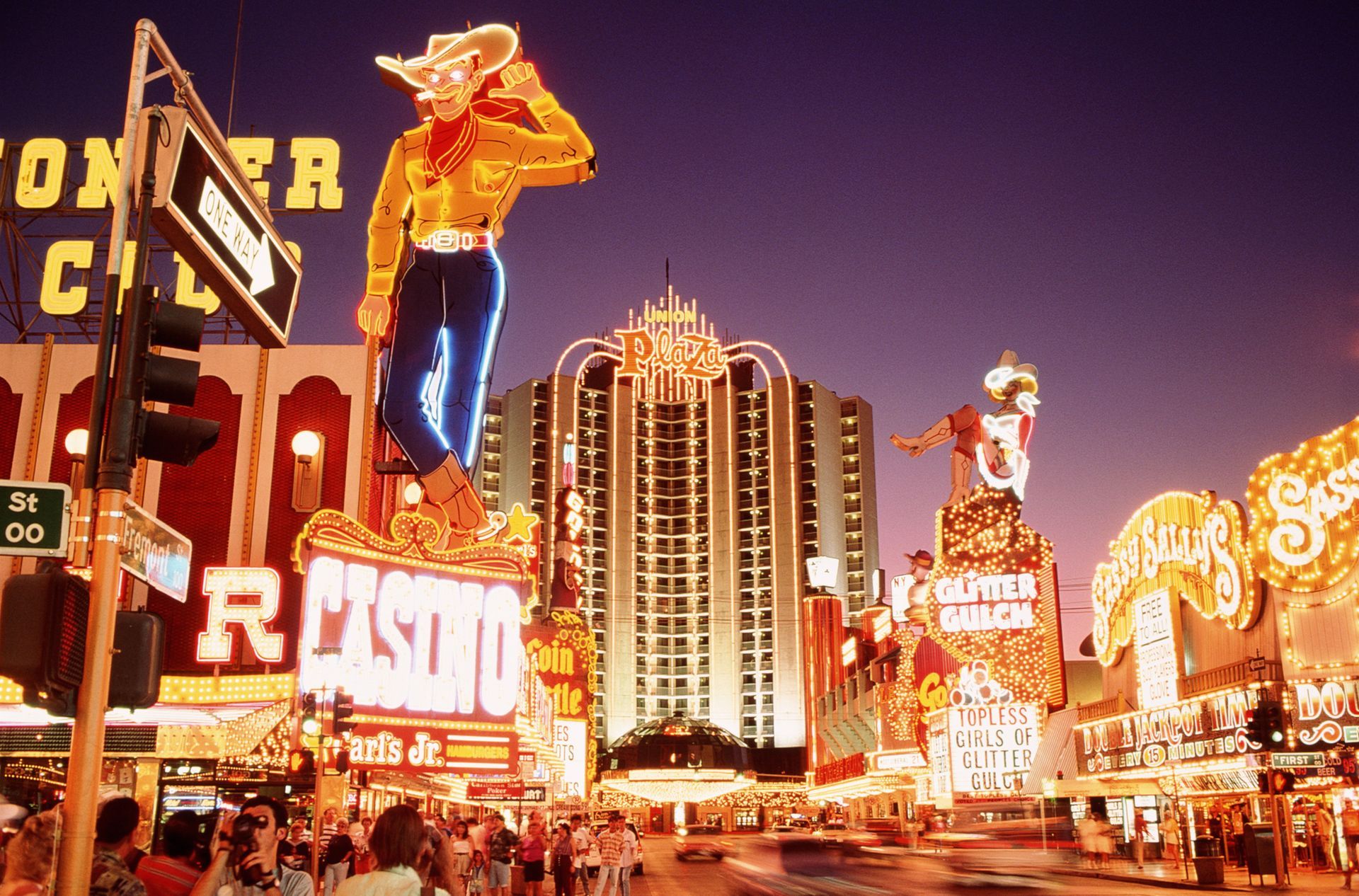 Neon cowboy sign on Fremont Street in Las Vegas, with casinos and street scene at dusk. Neon cowboy sign on Fremont Street in Las Vegas, with casinos and street scene at dusk.