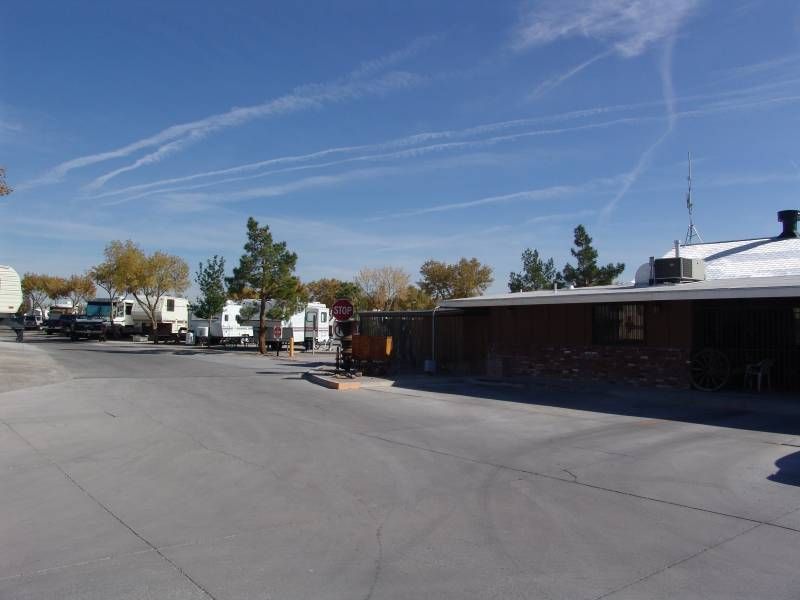 RV park with parked vehicles and a brick building under a blue sky with contrails.