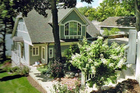 Suburban townhouse with gray siding, small front yard, and an American flag by a sunny sidewalk