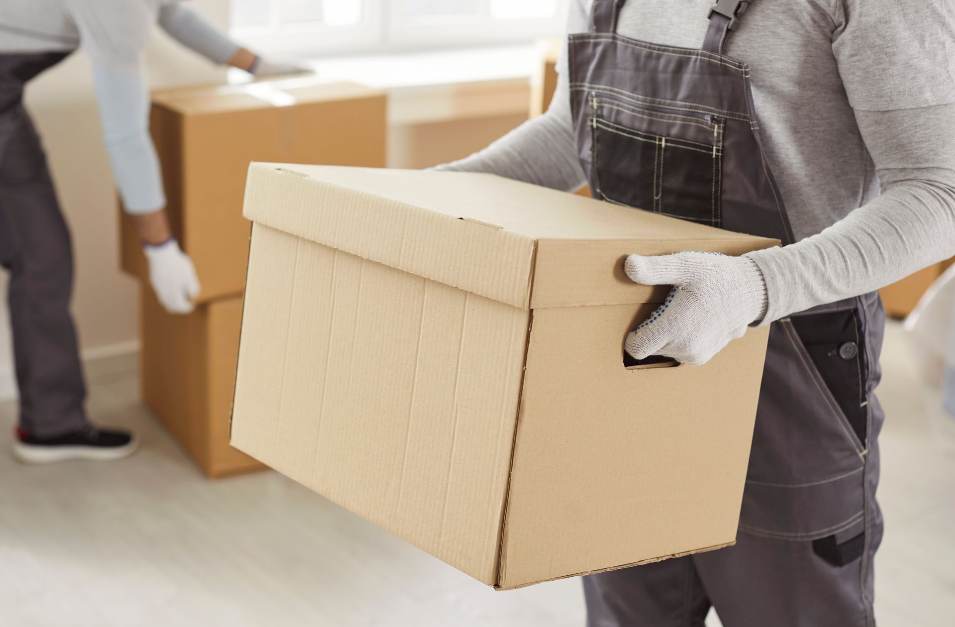 Movers in work gloves carrying cardboard boxes during a move